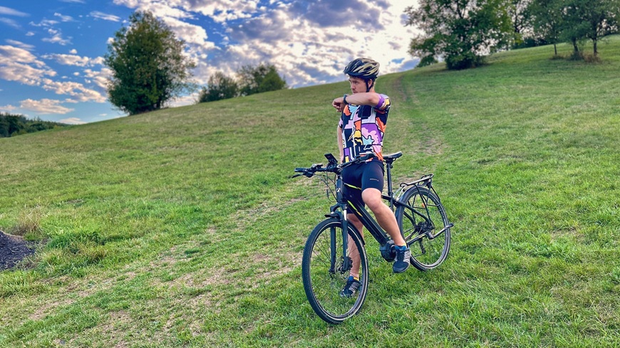 Muž na terénnom bicykli pri zastávke v prírode využíva hovor zo zápästia prostredníctvom inteligentných hodiniek Garmin fēnix® 9 Pro