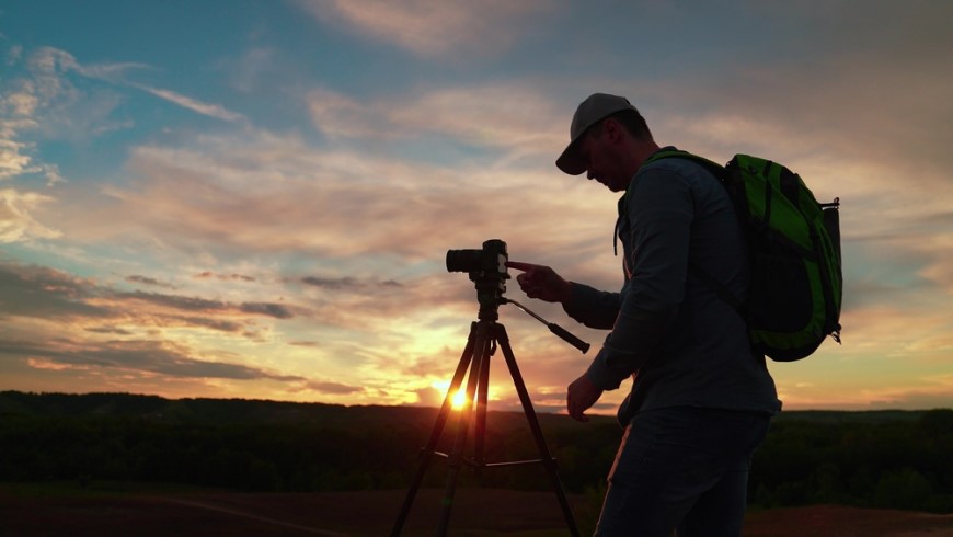 Jak vybrat stativ na mobil, fotoaparát či kameru? Muž fotografuje západ slnka digitálnym fotoaparátom na statíve.