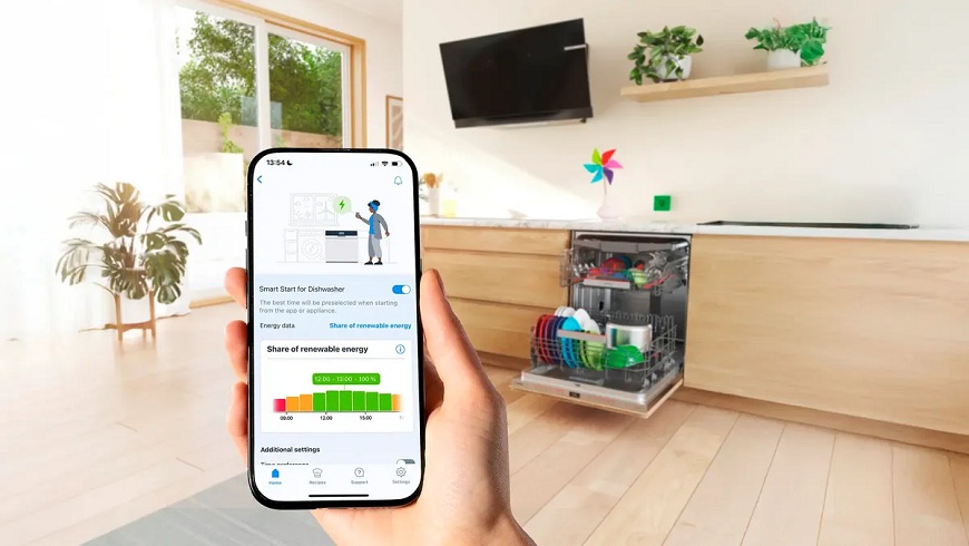 Ruka držiaca mobil s otvorenou funkciou Smart start, v pozadí umývačka Bosch