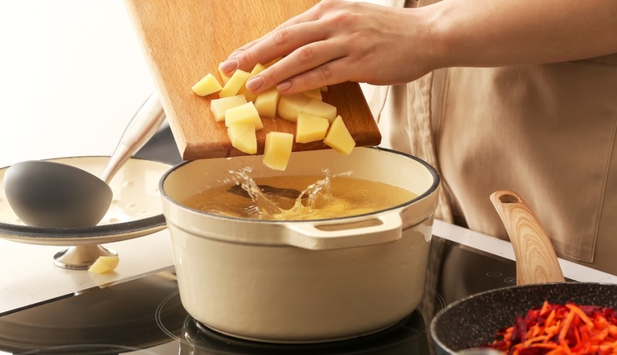 Ako dlho sa varia zemiaky, aby boli dokonalo mäkké Ruka zhŕňa nakrájané zemiaky z dosky do hrnca.