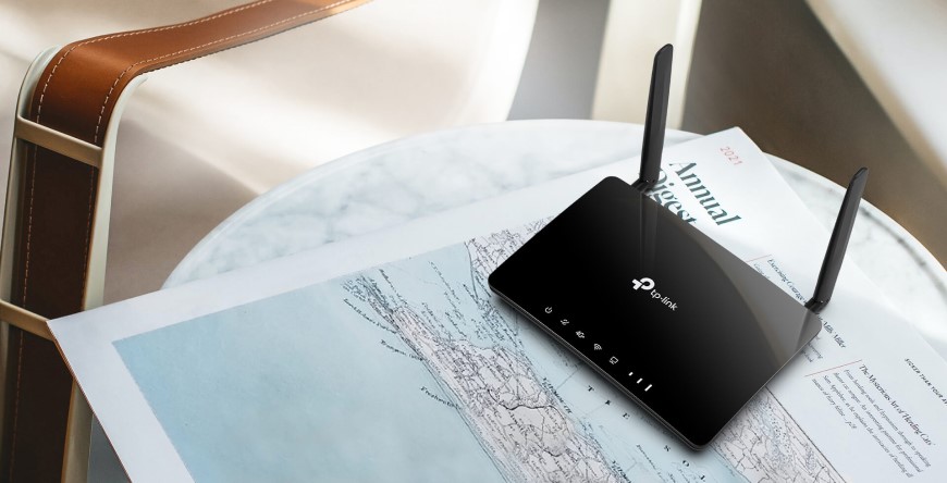 Ako vybrať router? Čierny Wi-Fi router položený na stolíku na novinách v obývačke.