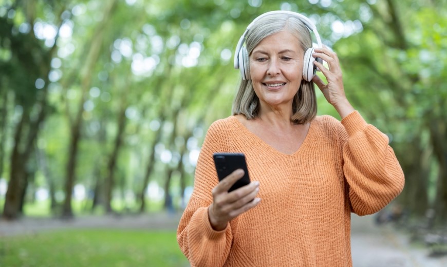 Najlepšie mobily pre seniorov Staršia žena v parku má na ušiach slúchadlá a mení hudbu prostredníctvom mobilného telefónu.