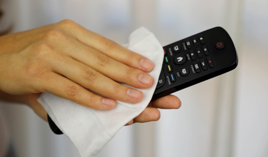 detail ruky utierajúcej diaľkový ovládač od televízora antibakteriálnym obrúskom