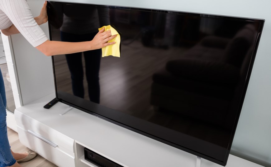žena utiera žltou handričkou televíznu obrazovku