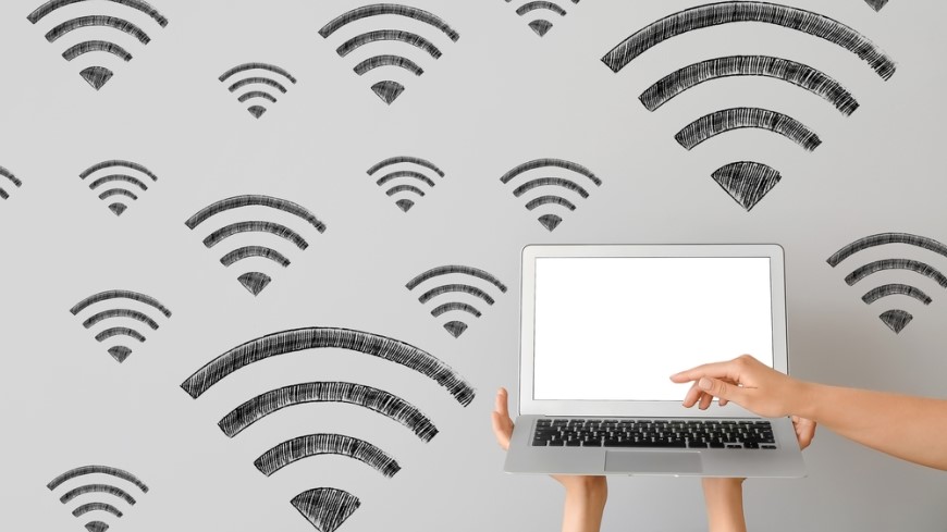 Ako prepojiť dva routery? laptop položený na rukách a pozadie steny s wi-fi symbolmi