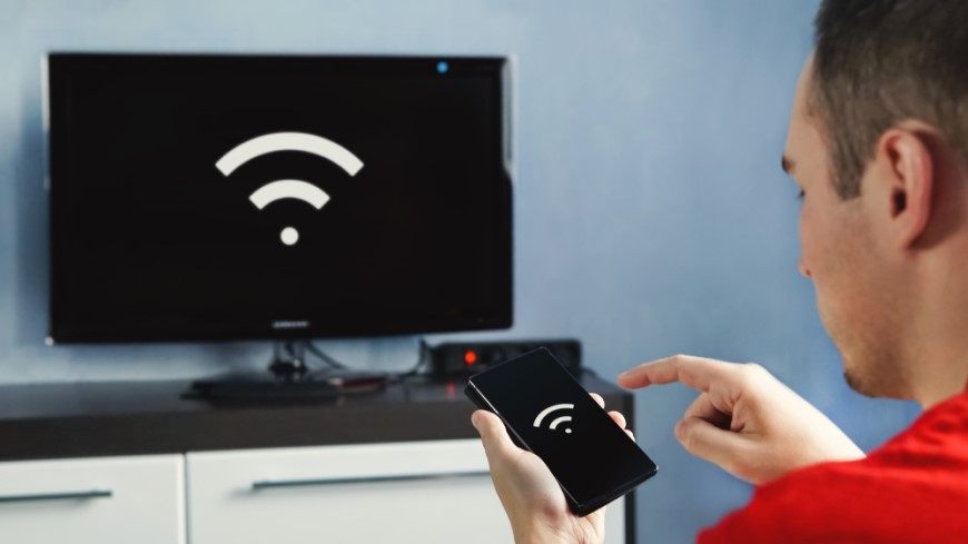 Ako pripojiť TV k Wi-Fi? muz s mobilom v ruke, pred sebou má televízor na komode