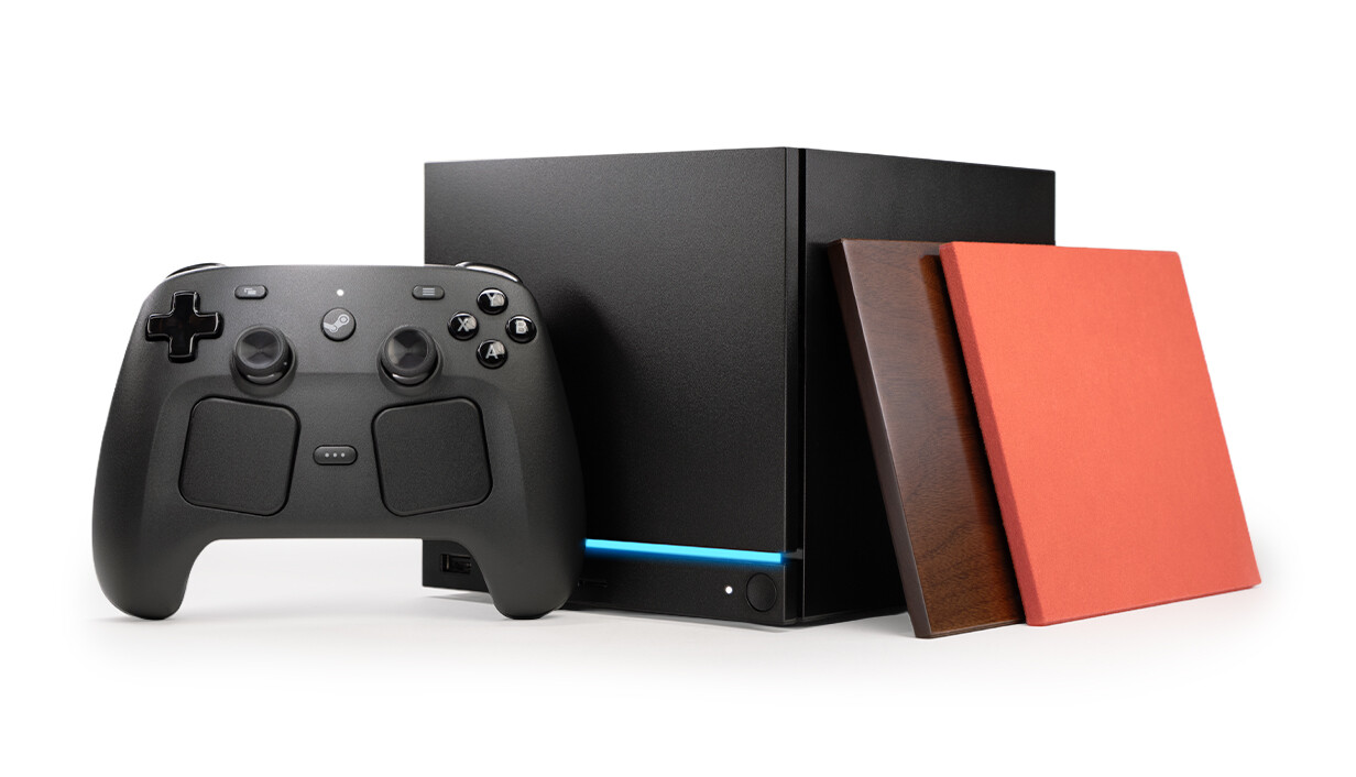 Steam Machine 2 TB, vedle je ovladač Steam Controller, o Steam Machine jsou opřeny dva náhradní kryty (červený a v provedení masiv ořech)