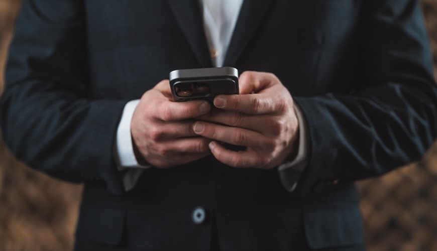 muž v obleku drži v rukách čierny iPhone