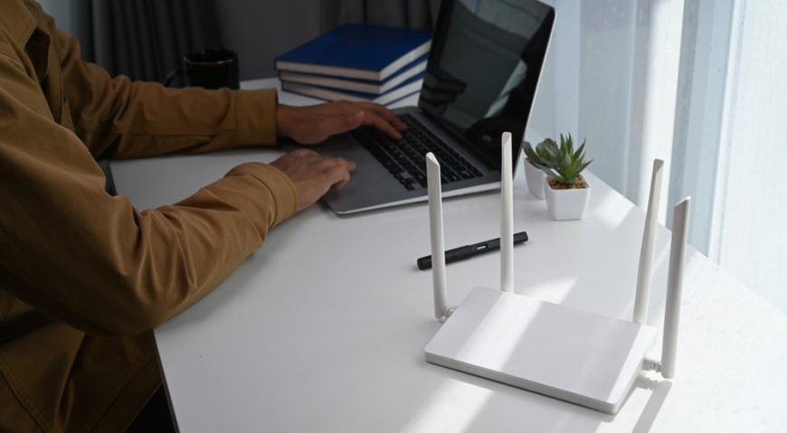 Osoba sediaca pri stole s notebookom a wi-fi routerom