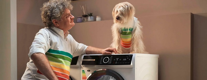 Sušte s novou sériou Bosch Serie 8 muž je opretý o sušičku bielizne Bosch Serie 8 a pozerá na psa, ktorý na nej sedí, obaja majú tričká s farbami symbolizujúcimi radenie energetických tried