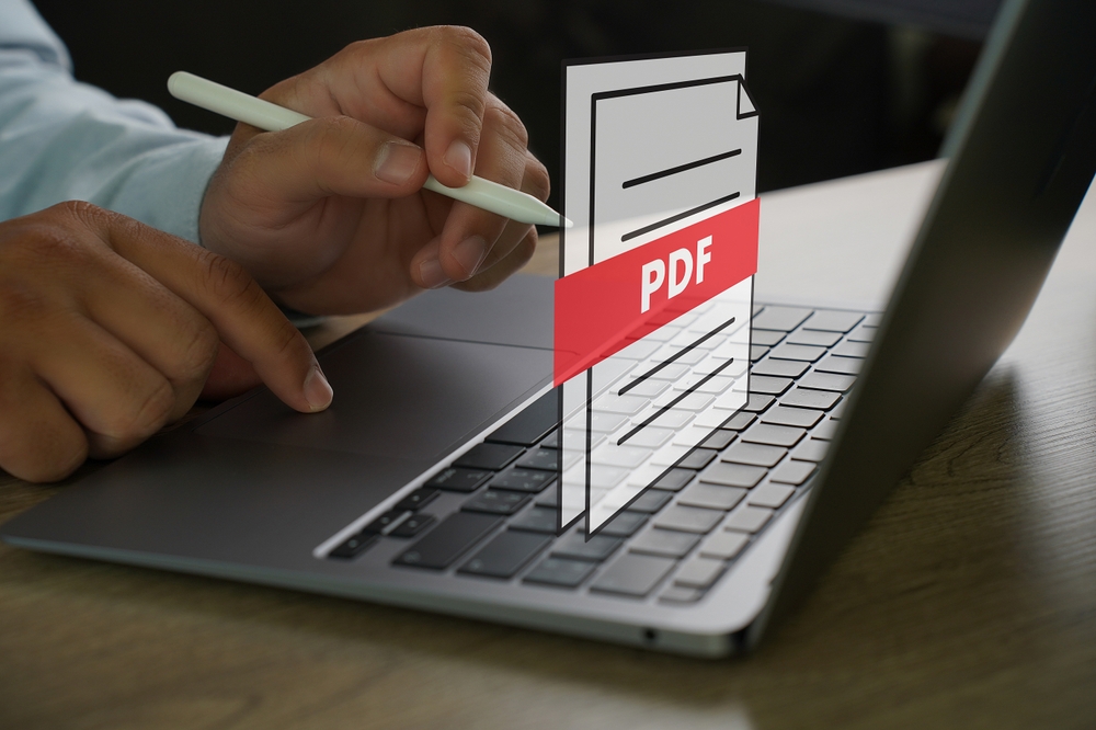 Ruky nad klávesnicou noteboooku s grafickou ikonou súboru PDF.
