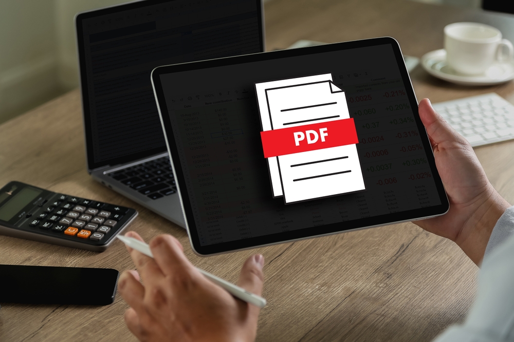 Pracujúci človek drží tablet, na ktorého obrazovke je grafická ikona súboru PDF-.