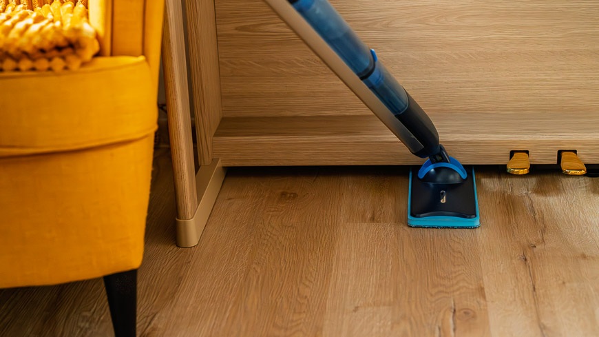 Mop Philips OneUp zasunutý pod klavírom. V rohu časť žltého kresla.