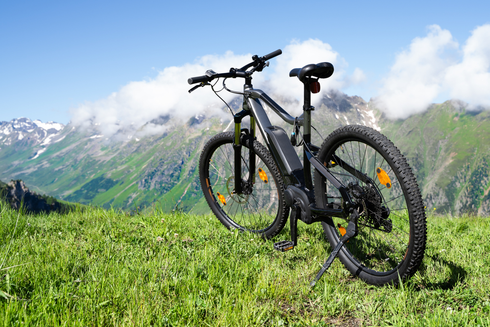 Elektrobicykel stoj´í na stojane na vrchu lúky s výhľadom na hory.