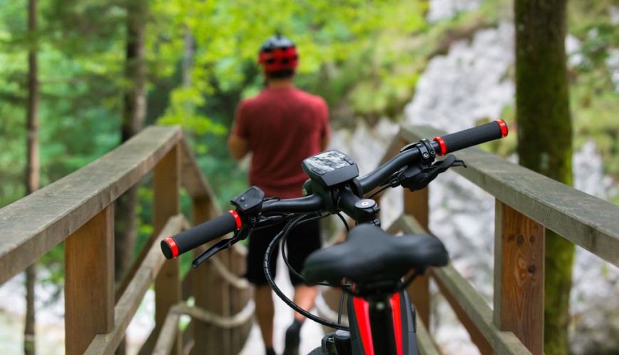 Ako vybrať elektrobicykel? muž v cykloodeve stojí na moste, bicykel je ostro vyobrazený v popredí fotografie
