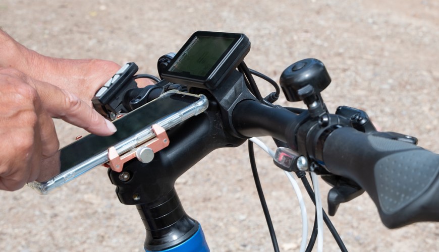 Ako vybrať elektrobicykel? Človek ovláda smartfón upevnený na riadidlách elektrobicykla