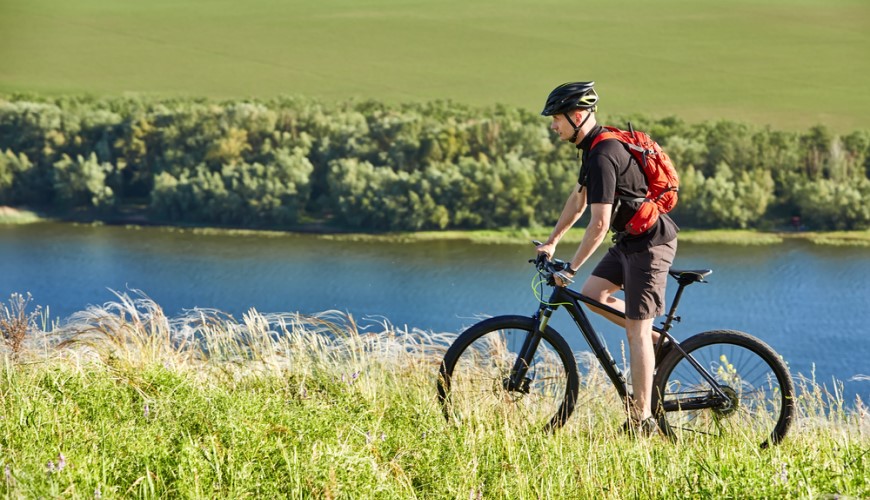 Muž jazdí na elektrobicykli po lúke popri rieke.