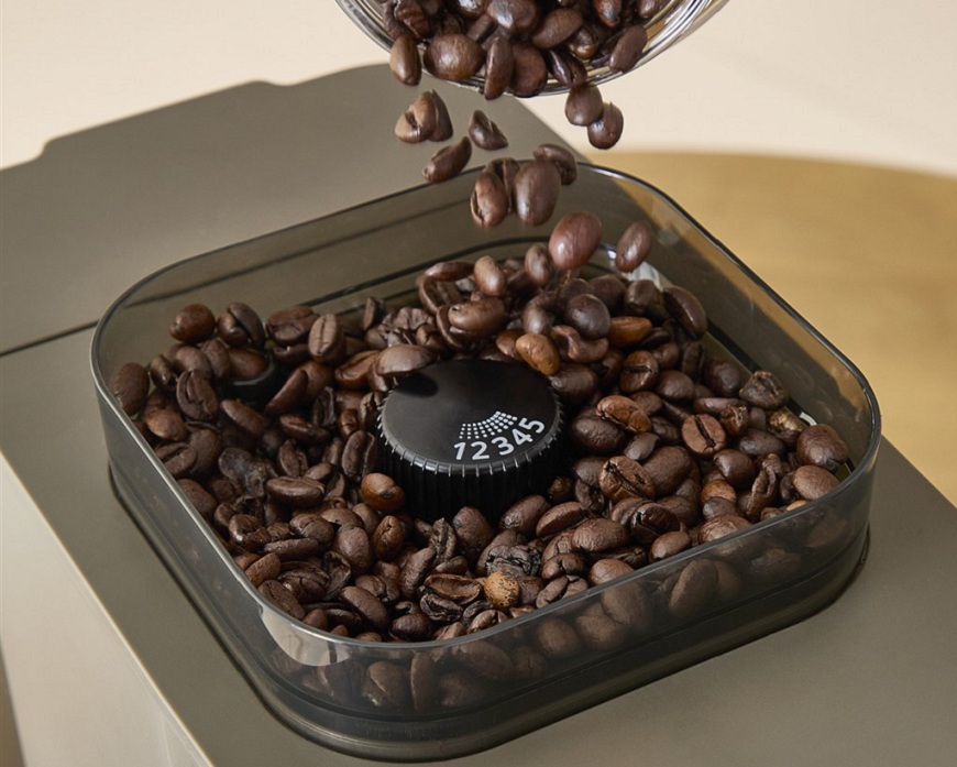 Detail na mlynček kávovaru Krups Coffee Crush Experience. Vnútri mlynčeka je zrnková káva a regulačné koliesko jemnosti mletia.