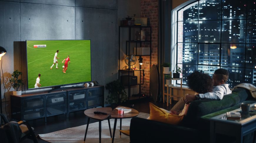 Najčastejšie televízne skratky a technológie Pár sedí na gauči a sleduje futbalový zápas na televízore.