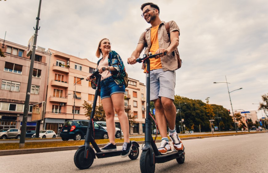 Ako vybrať elektrokolobežku? mladý muž a mladá žena idú na kolobežke po ceste cez mesto