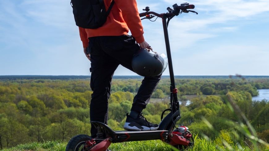 Ako vybrať elektrokolobežku? muž stojí na elektrokolobežke v turistickom oblečení na vrchole kopca v zalesnenej krajine
