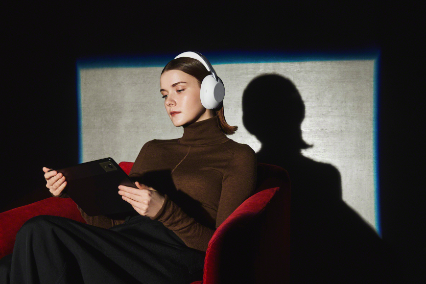 Žena sedí v červenom kresle, pozerá do tabletu a má nasadené slúchadlá Sony 1000X THE COLLEXION.