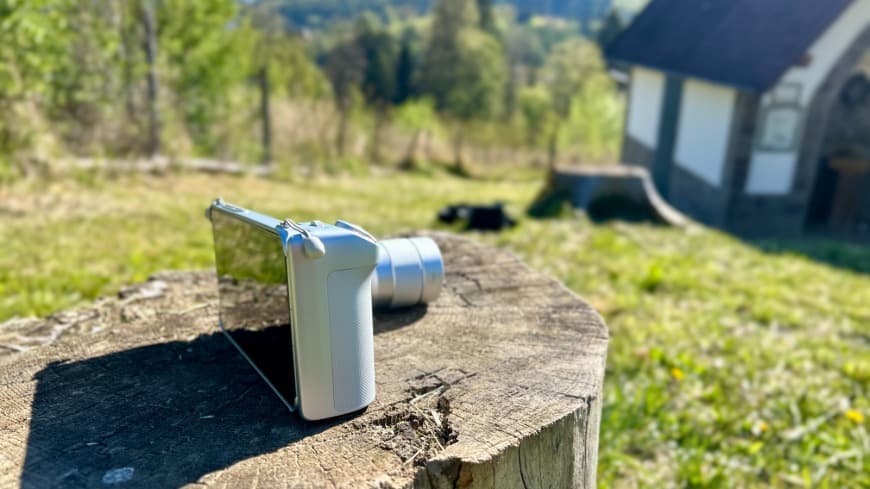Bočný pohľad na smartfón vivo X300 Ultra s nasadeným Imaging Gripom, položený na pni v teréne.