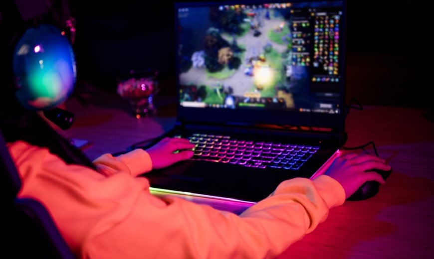 HDMI 2.2 – všetko, čo potrebujete vedieť o novom štandarde! gamer so slúchadlami na ušiach sedí za PC a hrá hru, klávesnica má RGB podsvietenie, izba je stlmená a osvietená rovnako v RGB farebných odtieňoch, pohľad od chrbta