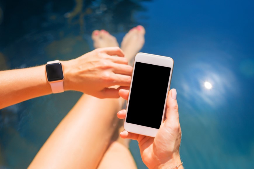 žena v športovom oblečení sedí na zemi a pozerá na Apple Watch na ruke a iPhone, ktorý drží v druhej ruke