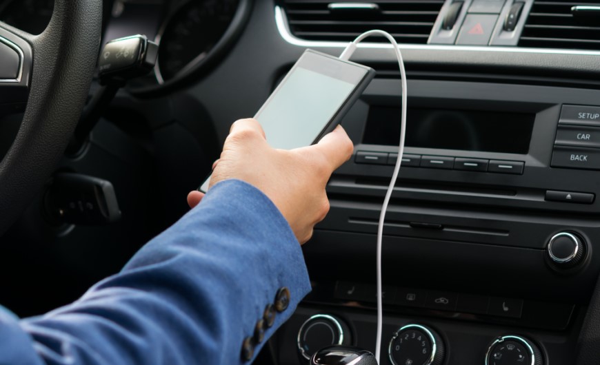 Ako spárovať telefón s autom: Sprievodca, s ktorým to zvládnete za 2 minúty Muž sedí v aute na mieste vodiča a má pripojený chytrý telefón cez kábel k autu