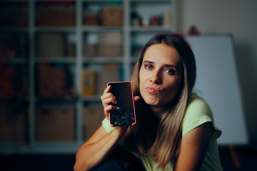žena so znepokojivým výrazom tváre kvôli prasknutiu displeja na telefóne, ktorý drží v ruke