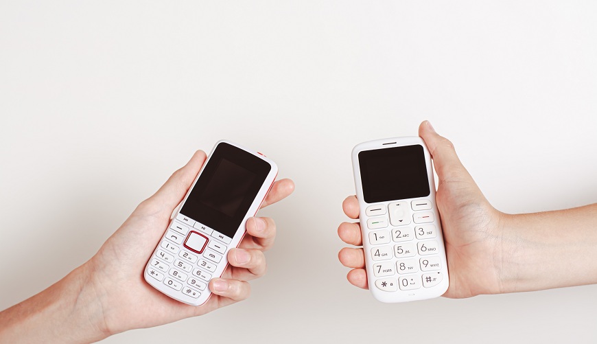 Dva biele tlačidlové mobilné telefóny v rukách