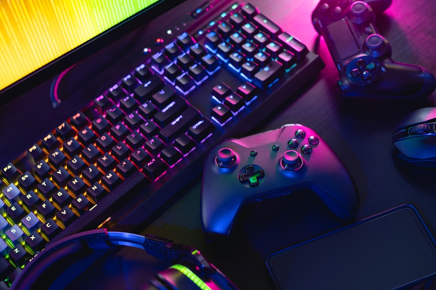 Prázdniny 2026 hrou: Odmeňte gamera za vysvedčenie! Na stole leží pred monitorom klávesnica, 2 gamepady a myš