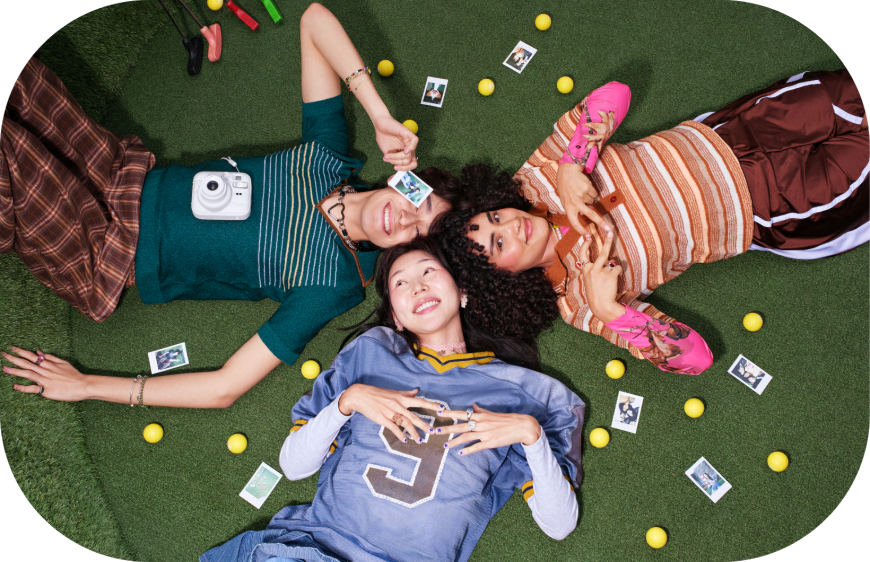 Tři teen-kamarádi leží na zemi, fotí se na instax mini 13 a kolem nich jsou fotografie