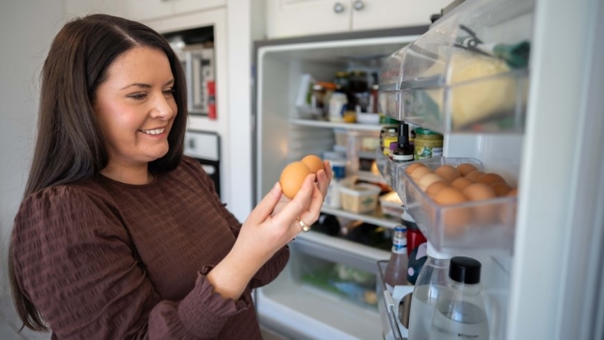 Ako správne usporiadať chladničku? žena drží v ruke vajíčka, ktoré vybrala s chladničky a teší sa im