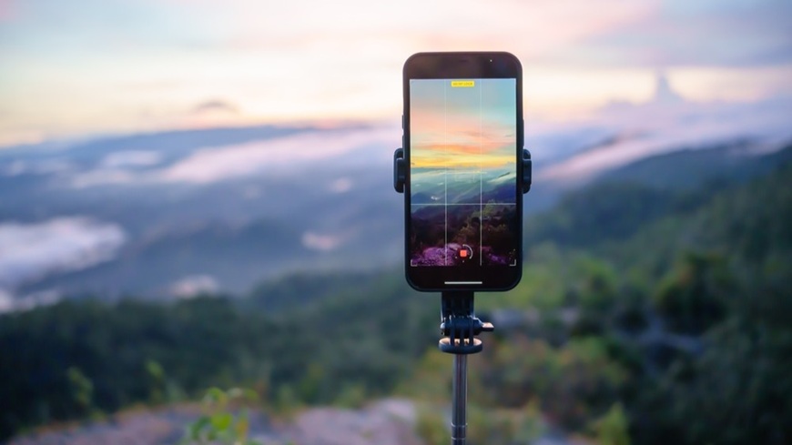 Mobilní telefon, usazený na stativu, při fotografování večerní krajiny v pozadí