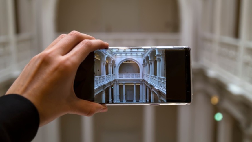Symetrická kompozícia v praxi – fotografovanie architektonických prvkov – stĺporadia a klenutých oblúkov – smartfónom v mužskej ruke.