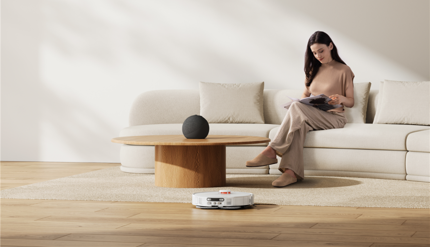 Žena si číta na gauči a pred ňou vysáva obývaciu izbu robotický vysávač Xiaomi Robot Vacuum H50 Pro