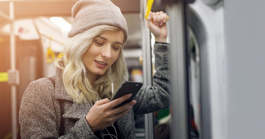 Slúchadlá ako vaša osobná audio bublina: Ako si vybrať tie správne do mesta, práce aj na cestovanie žena v zimnom oblečení počúva hudbu v električke cez slúchadlá a pozerá do smartfónu