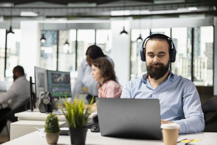 Slúchadlá ako vaša osobná audio bublina: Ako si vybrať tie správne do mesta, práce aj na cestovanie muž sedí v kancelárii so slúchadlami na ušiach a pracuje na počítači