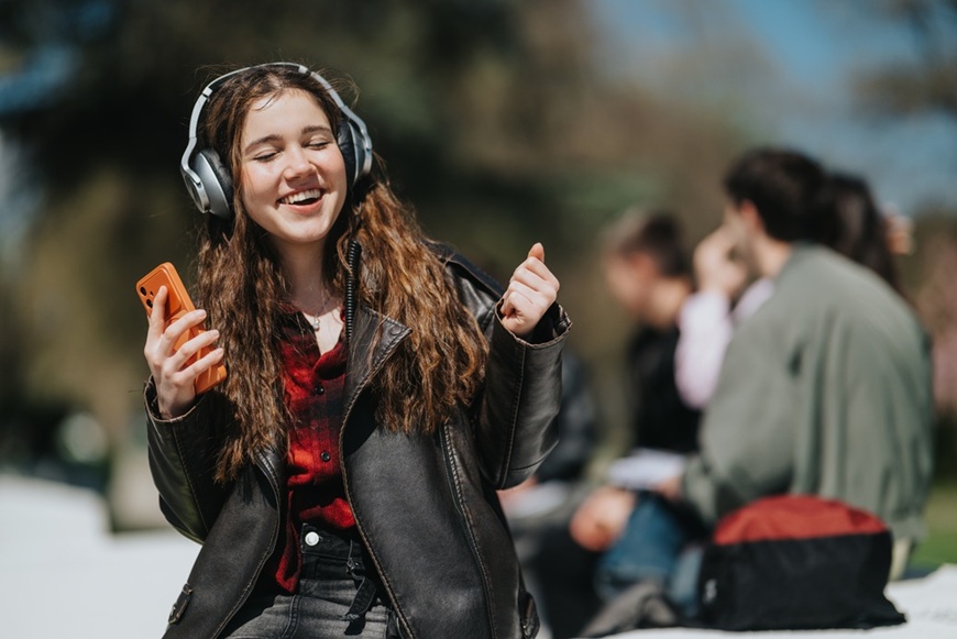 Slúchadlá ako vaša osobná audio bublina: Ako si vybrať tie správne do mesta, práce aj na cestovanie šťastná mladá žena sedí na múriku v meste užíva si počúvanie hudby cez slúchadlá