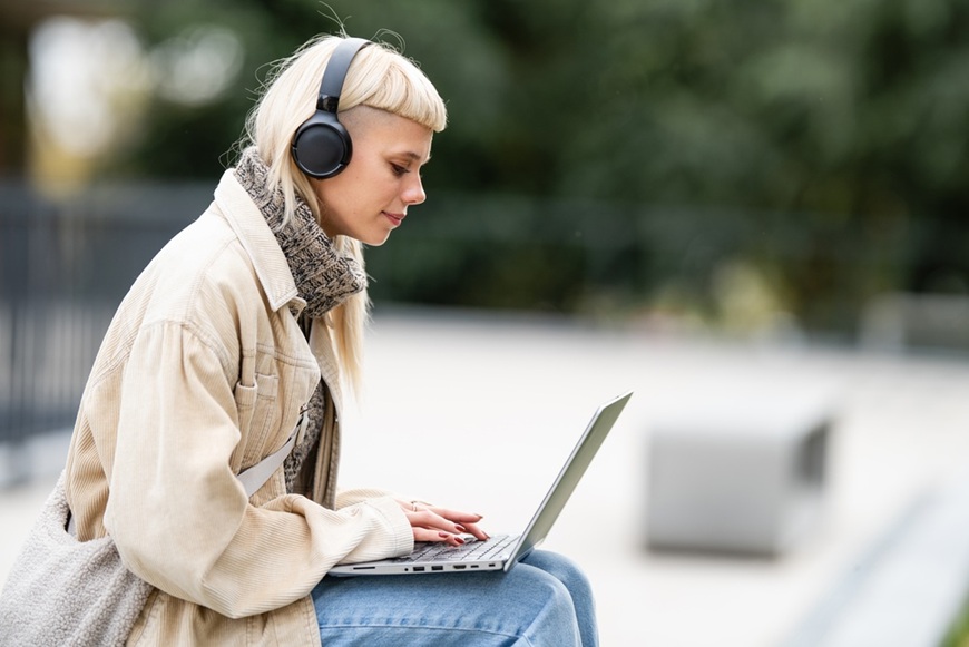 Slúchadlá ako vaša osobná audio bublina: Ako si vybrať tie správne do mesta, práce aj na cestovanie mladá žena sedí na múriku v meste a počúva hudbu cez slúchadlá