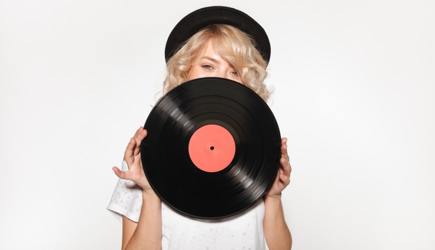 dievča s klobúkom drží vinylovú dosku pred svojou tvárou
