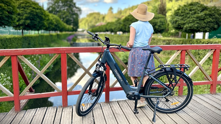 Recenzia: Elektrobicykel GoGEN Aspen MX 720 sa postará o to, aby vaše cyklistické túžby nič nebrzdilo Elektrobicykel GoGEN Aspen MX 720 stojaci na moste pred ženou v elegantnom klobúku, ktorá sleduje tečúci potok v pozadí