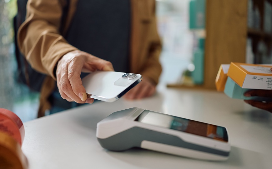 Ako platiť mobilným telefónom? Muž prikladá mobilný telefón k platobnému terminálu.