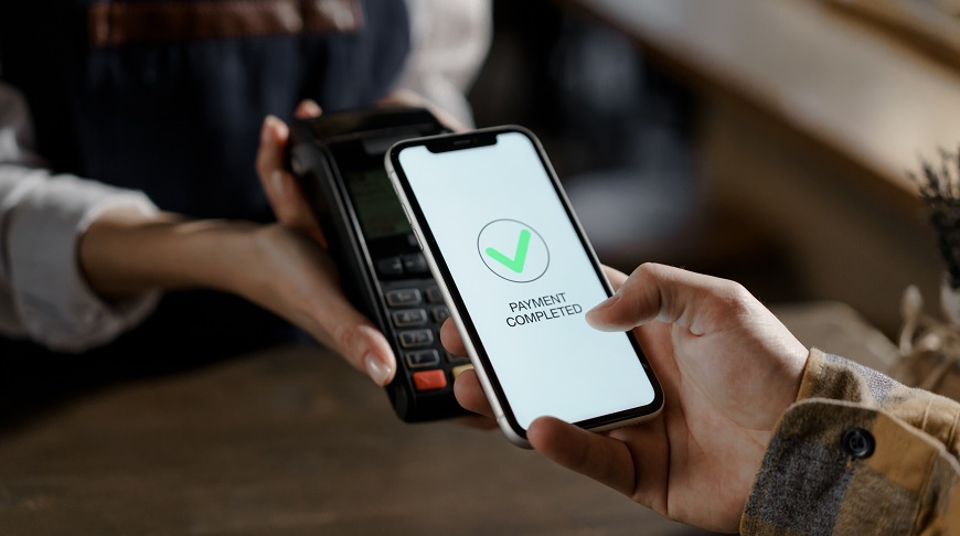 Ako platiť mobilným telefónom? Muž prikladá mobil k terminálu a na displeji svieti oznámenie o schválení platby.