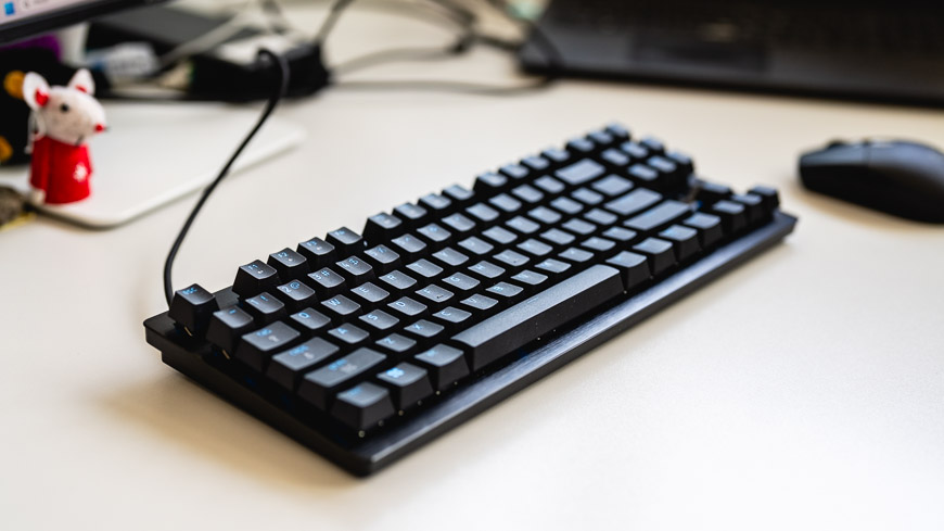 Herná klávesnica Razer Huntsman Tenkeyless V3 8KHz leží na stole, na pozadí je počítačová myš, stojan monitora a figúrka myšky