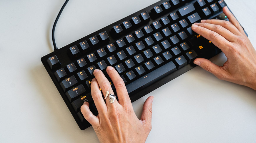 Herná klávesnica Razer Huntsman Tenkeyless V3 8KHz s oranžovým podsvietením leží na stole, na klávesnici sú položené ruky