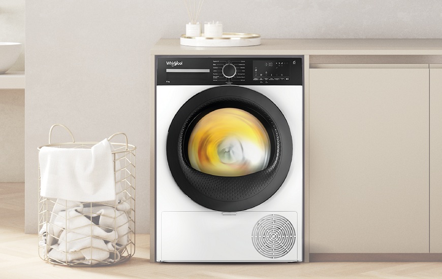 Sychravá jeseň sušeniu bielizne nepraje. Sušičky Whirlpool áno! Sušička Whirlpool s bubnom plným bielizne. Vedľa sušičky je kôš na bielizeň.