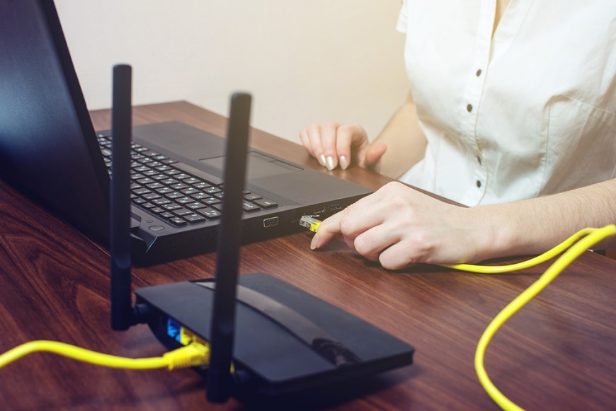 Ako pripojiť notebook k internetu? Žena prepája notebook a router pomocou ethernetového kábla.